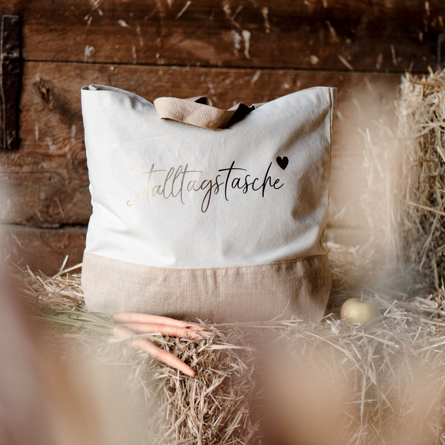 Helle Jutetasche mit schwarz-goldenem Motiv auf Stroh im Stall 