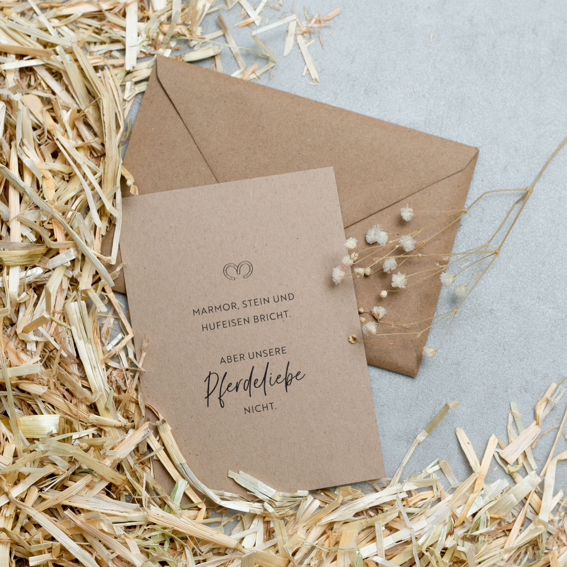 Kraftpapier Postkarte mit Kraftpapier Umschlag auf Stroh und grauem Untergrund 